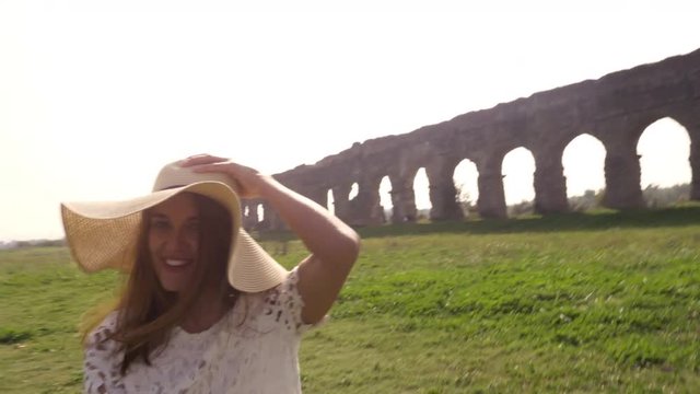 Come with me. Young beautiful girl with hat leading man boyfriend holding hands toward roman aqueduct arches in parco degli acquedotti park ruins in rome romantic lovely happy couple slow motion