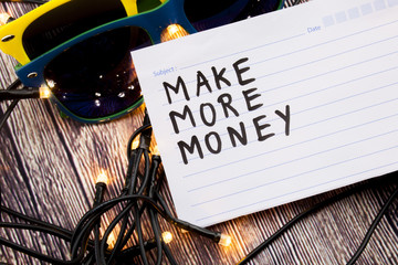 Make more money handwritten on a registers page with black color. Two sunglasses in various combinations of colors with lights set in the random order with wooden background. Business concept.