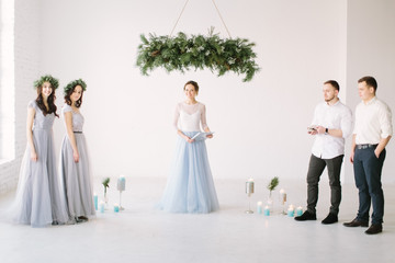 Young woman speech master in white blue dress standing under the pine arch together with bridesmaids and groommen before the wedding ceremony.