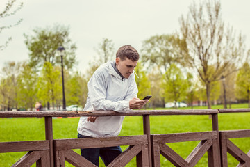 Fototapeta premium Молодой парень стоит на мосту, мужчина смотрит в телефон и читает сообщение