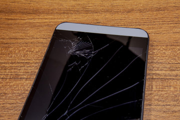 Black mobile phone on the wooden table with crashed lcd display. Mobile technology concept. Destroyed smartphone in closeup view. Crashed mobile phone on the table.