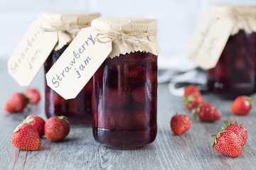Strawberry jam in glass jar on  gray background.
