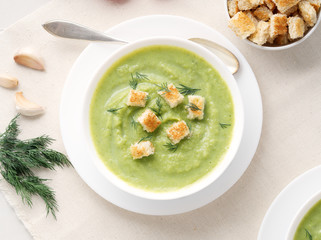 large white bowl with vegetable green cream soup of broccoli, zucchini, green peas on white background, top view