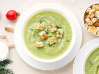 large white bowl with vegetable green cream soup of broccoli, zucchini, green peas on white background, top view