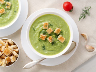 Two large white bowl with vegetable green cream soup of broccoli, zucchini, green peas on white background, top view