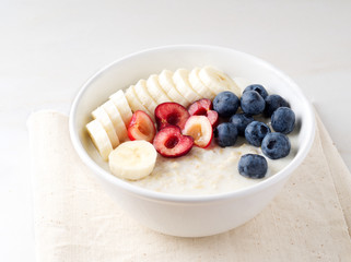 Large bowl of tasty and healthy oatmeal with fruits and berry for Breakfast, morning meal. Side view, white marble table