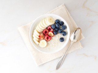 Large bowl of tasty and healthy oatmeal with fruits and berry for Breakfast, morning meal. Top view, white marble table