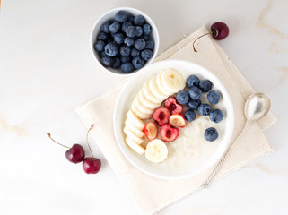 Large bowl of tasty and healthy oatmeal with fruits and berry for Breakfast, morning meal. Top view, white marble table