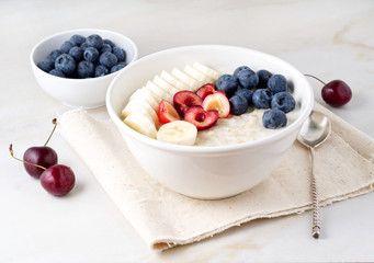 Large bowl of tasty and healthy oatmeal with fruits and berry for Breakfast, morning meal. Side view, white marble table