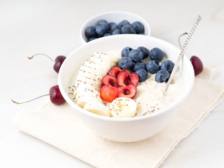 Large bowl of tasty and healthy oatmeal with fruits and berry for Breakfast, morning meal. Side view, white marble table