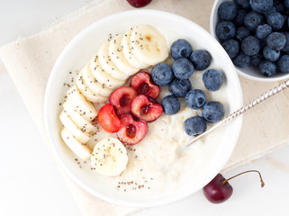 Large bowl of tasty and healthy oatmeal with fruits and berry for Breakfast, morning meal. Top view, white marble table