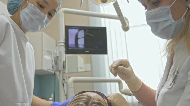 Doctor used special Dental Intraoral Check Digital Micro Camera to exam teeth. On the monitor dentist and patient see video of teeth, tooth problems. Doctor and assistant work in protective masks