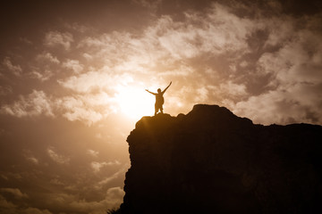 Stand strong. Man with arms in the air standing on top a mountain. Feeling motivated, strength and courage concept.