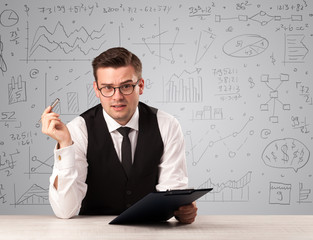 Young handsome businessman sitting at a desk with white charts behind him