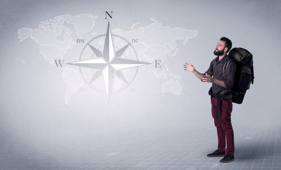 Handsome young man standing with a backpack on his back and a compass and a world map in the background