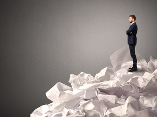 Thoughtful young businessman standing on a pile of crumpled paper with a deep grey background