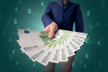 Young businessman holding large amount of bills with green background and currency symbols 