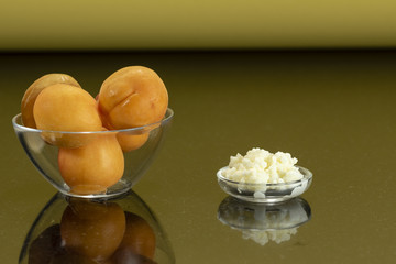 glass bottles with a homemade apricot smoothie with kefir yogurt, fresh milk, a glass plate with kefir grains, a glass plate with apricots and surface reflection, yellow gold orange background