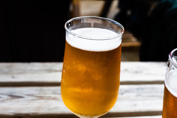 Glass of beer on the wooden table. Draft beer served at the bar. Glass of light beer on the wooden board. Served alcoholic drinks in a glass. Alcoholic beverage with blurred background.