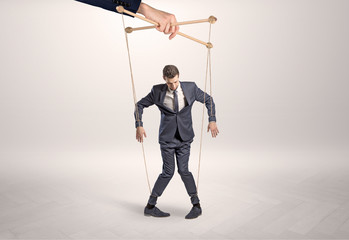 Puppet businessman in an empty room leaded by a huge hand
