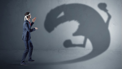 Businessman with boxing glove fighting with a big monster shadow
