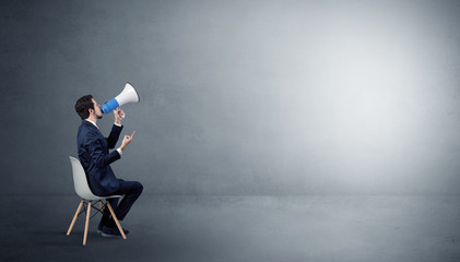 Businessman staying in an empty grey dark room with stuffs on his lap
