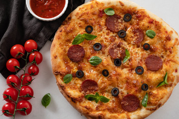 Hot pepperoni pizza on white stone background. Tasty pizza with salami, cheese and tomatoes on white table, top view