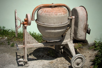 Dirty mini cement mixer in the the ground with little rocks and stones and tall green grasses...
