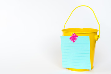 Illustration of bucket list concept with yellow metal bucket and list taped to front against white background