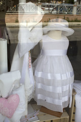 Fototapeta na wymiar A nice baby girl white dress and ribbon displayed from a shop. The wardrobe is top with a hat and striped with a silk. It is exhibited or parade in the botique for the customer to see.