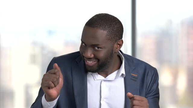 Funny dark-skinned man in formal wear. Cheerful black man in business suit inviting for a dance on blurred background. Lets dance concept.