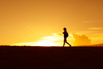 Silhouette of female backpacker walking cross country. Adventure, and travel concept. 