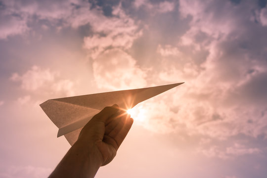 Hand holding paper airplane against sunset sky. Taking flight, and take off concept. 