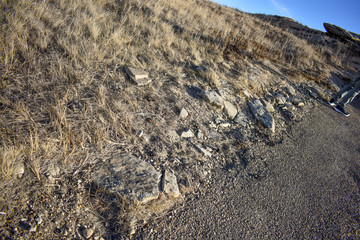 Feet of a hiker standing on a  dirt path running beside a small rocky hill covered partially in grass.