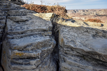 A distant scenic view of a small canyon range behind a tiny trench between two merging boulders.