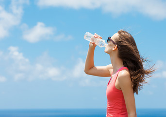Fit woman drinking bottle of water outdoors. 