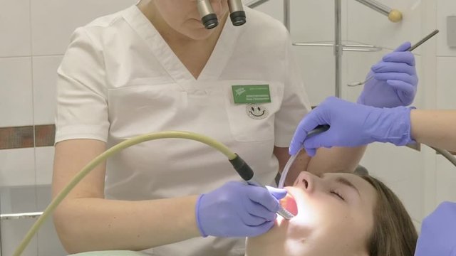 Woman at dentist clinic gets dental treatment to fill a cavity in a tooth. Dental restoration and composite material polymerization with UV light and laser. The doctor works with an assistant.