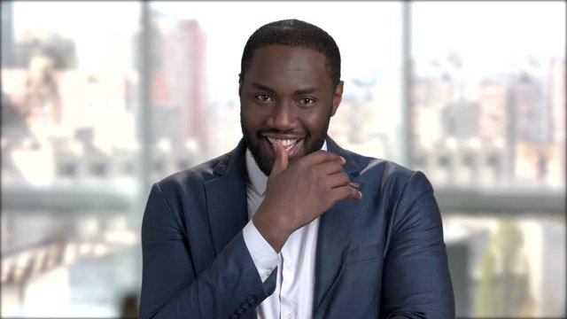 Sexy afro-american businessman is flirting. Handsome dark-skinned man in business suit is winking on blurred background.
