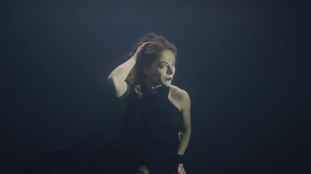 Attractive woman swimming under water in dark pool while video shooting