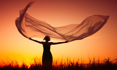 beautiful sunset fantasy girl. Woman holding scarf blowing in the wind.

