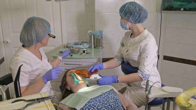 Woman at dentist clinic gets dental treatment to fill a cavity in a tooth. Dental restoration and composite material polymerization with UV light and laser. The doctor works with an assistant.