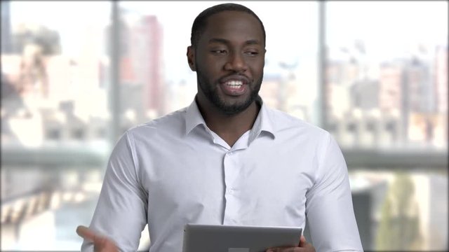 Black handsome manager using digital tablet. Afro-american business trainer holding computer tablet and talking to camera.