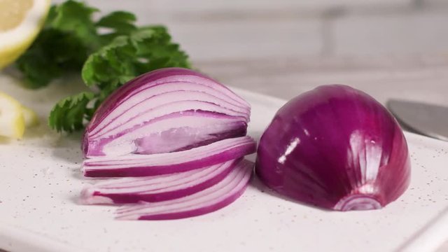 Sliced red onion, lemon and parsley leaves on white ceramic cutting board.