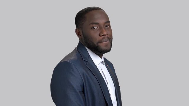 Black flirtatious businessman on grey background. Portrait of joyful dark-skinned macho-man. Invitation for a date gesture.