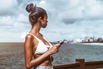 Young dazzling Brazilian female is standing with her smartphone on the observation point next to...