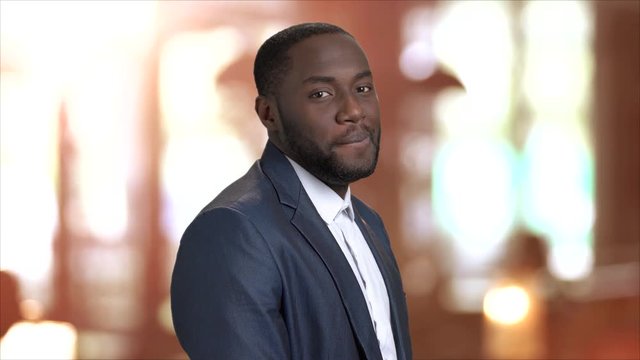 Attractive businessman is flirting on blurred background. Stylish afro-american macho man is smiling and flirting with you. Come to me gesture.