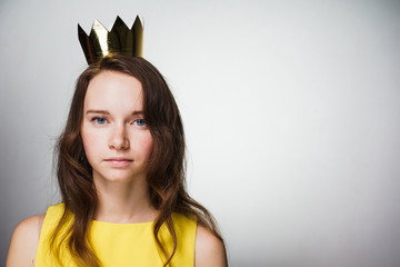 serious young blue-eyed girl in a yellow dress looks at the camera, on her head a golden crown