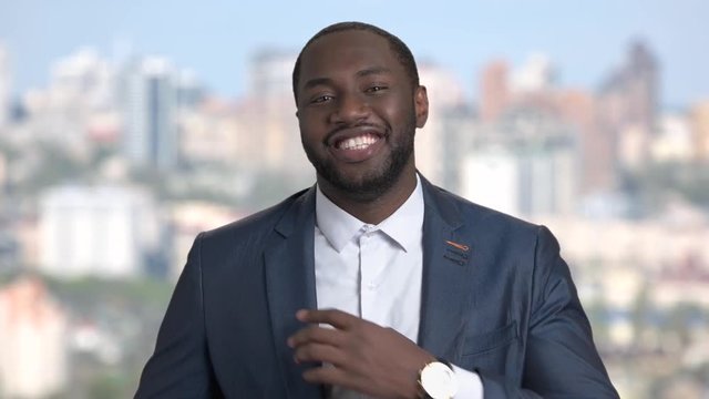 Smiling macho-man adjusting his suit. Cheerful african-american businessman adjusting his clothes on blurred background.