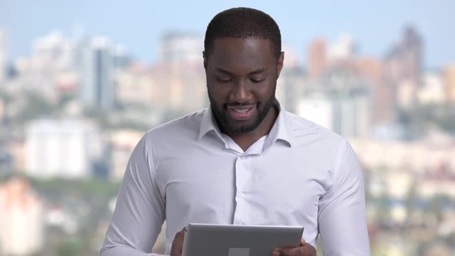 Smiling businessman using digital tablet. Handsome afro-american executive in white shirt working on cmputer tablet and smiling on blurred background.
