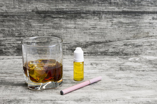 Whiskey in a glass with an e-cigarette and liquid for it on a gray stone background 
 